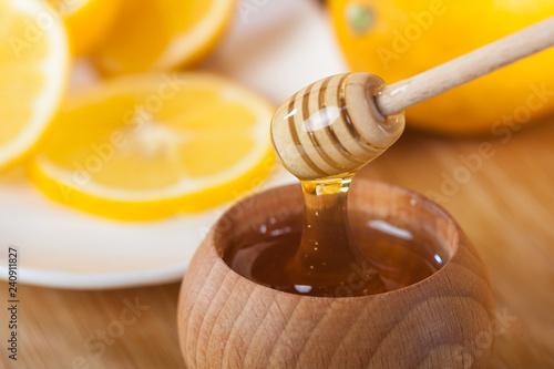 honey in a wooden bowl with honey dipper and lemon on a wooden kitchen board