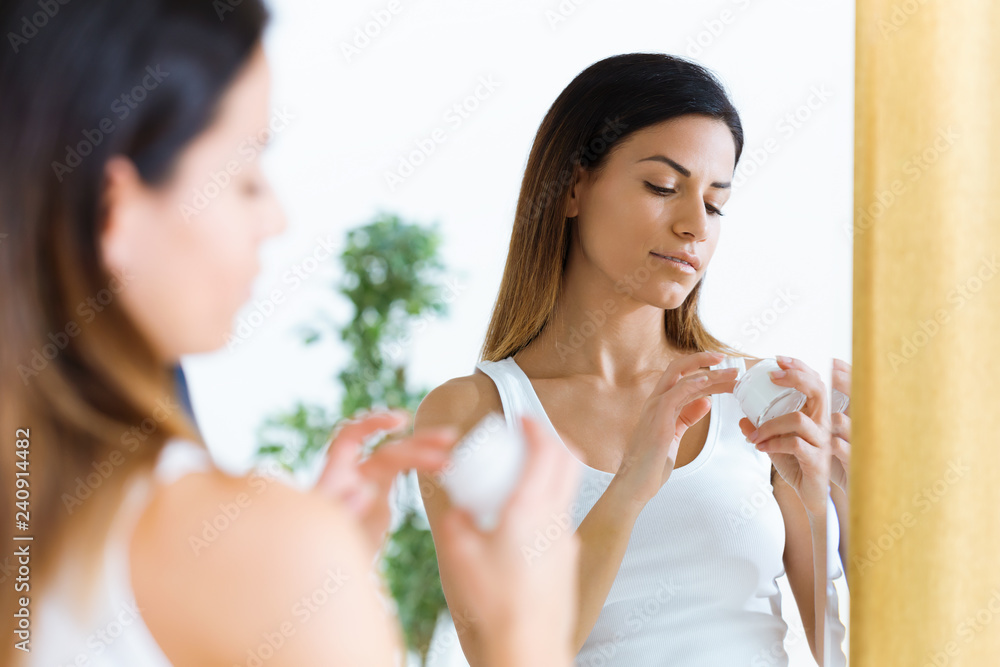 Beautiful young woman caring of her skin standing near mirror in the bathroom. Beautiful young woman caring of her skin standing near mirror in the bathroom.