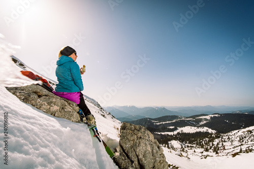 A ski tourer girl having a snack in the mountains in winter snowy landscape