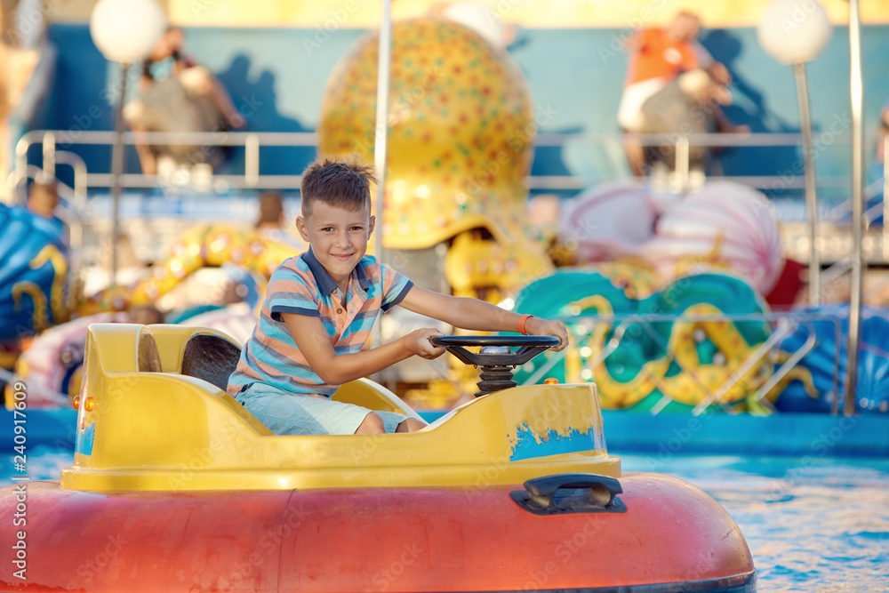 Cute European boy in striped t-shirt is driving water boat in the Luna park. He is enjoying his holidays and smiling to the camera.