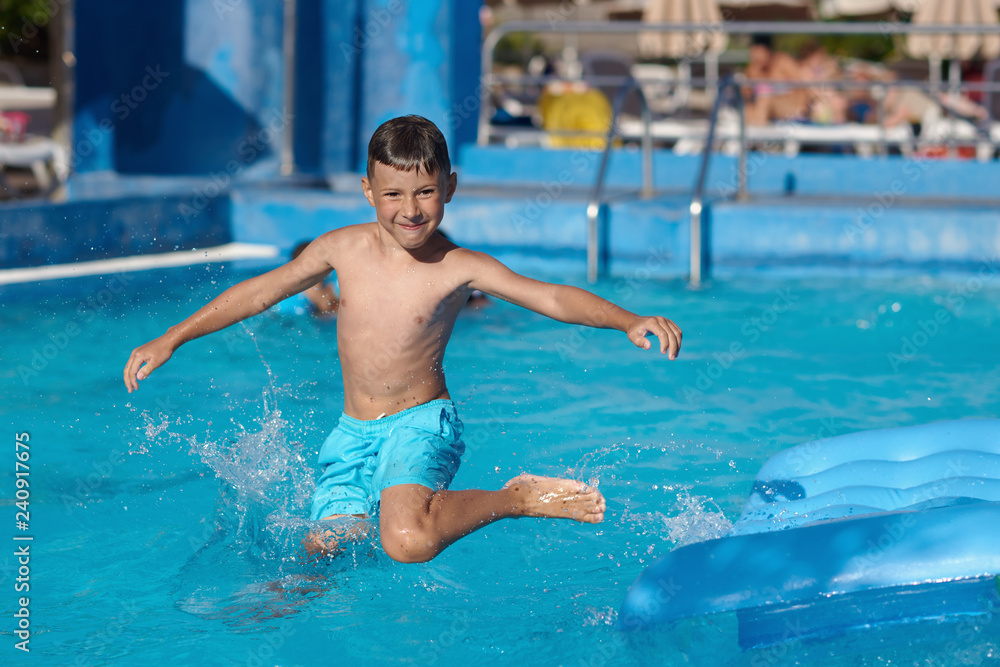 Caucasian boy having fun making fantastic jump into swimming pool at resort. He has wide open arms and crossed legs.