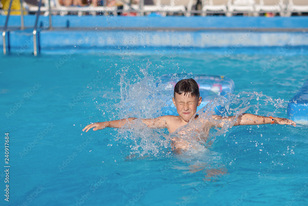 Cute European boy is diving from the inflatable blue floater into the hotel’s swimming pool. He is enjoying his summer vacations.