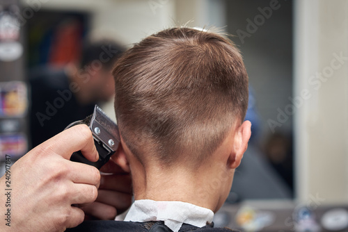 Back view of cute boy getting hairstyle by hairdresser in barbershop.