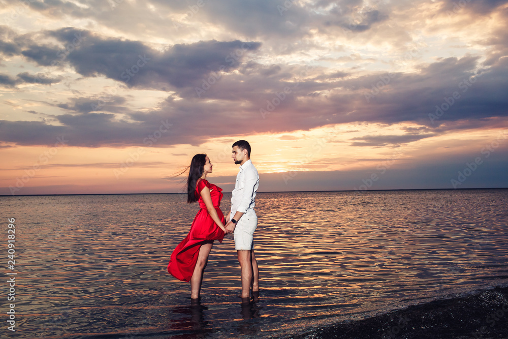 Fototapeta premium young couple in love holding hands in the sea against the backdrop of a beautiful sunset.