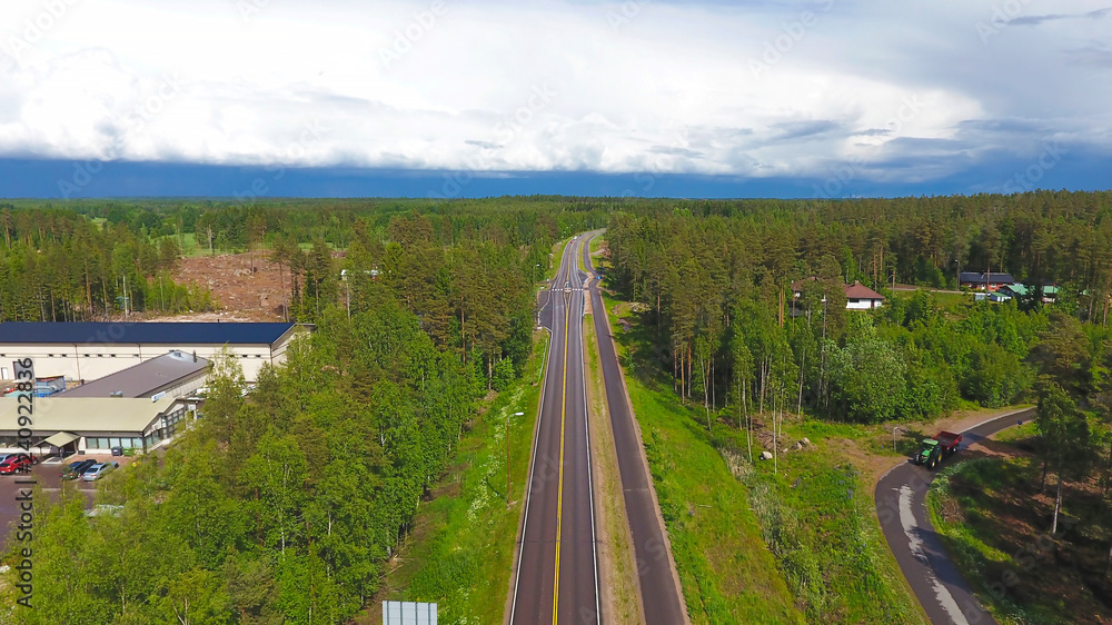 Summer aerial photography asphalt road in the countryside through the forest in Finland. Technical buildings and cars top view. The sky in the clouds and the horizon. Summer aerial photography asphalt road in the countryside through the forest in Finland. Technical buildings and cars top view. The sky in the clouds and the horizon.
