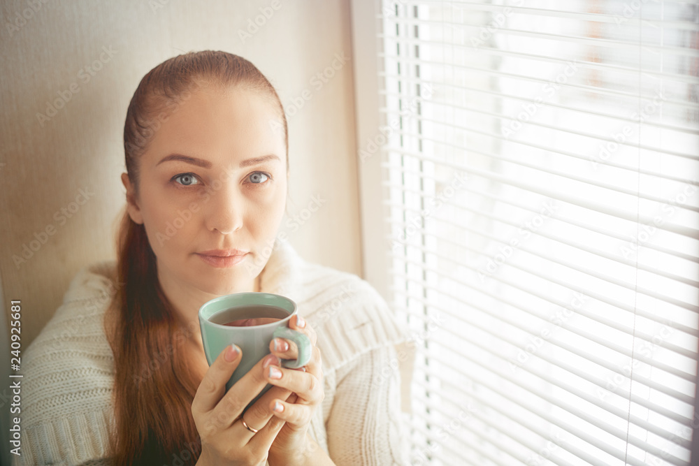drinking tea sitting on the window of Caucasian beautiful middle-aged woman with red hair, toning drinking tea sitting on the window of Caucasian beautiful middle-aged woman with red hair, toning