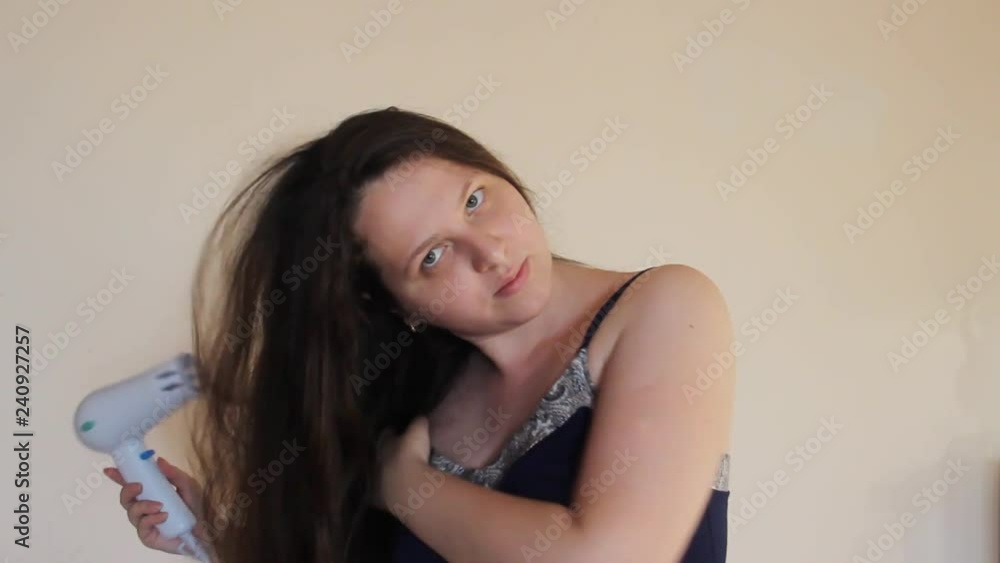 Brunette or brown-haired fat woman in a nightdress drying long hair with hairdryer at home against the yellow wall. blow-dry luxurious long hair Brunette or brown-haired fat woman in a nightdress drying long hair with hairdryer at home against the yellow wall. blow-dry luxurious long hair