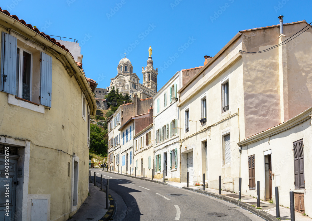 A narrow sloping street bordered with old townhouses in Marseille, France, going up to Notre-Dame de la Garde basilica on top of the hill.