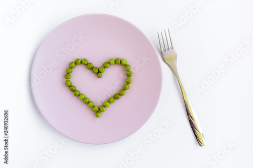 Green peas heart shaped, pink plate and a fork on white table. St. Valentine's day concept © ReaLiia