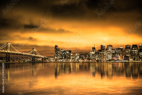 View of San Francisco skyline under golden sunset sky with lights and Bay Bridge