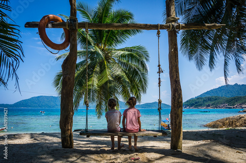 Kids staring at the ocean on a swing at the beach of Perhentian island, a tropical paradise in Malaysia photo