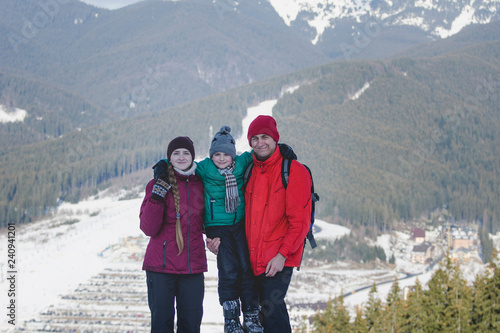 Mother, father and son are standing and smiling against the background of snow-capped mountains. Happy family. Winter day.