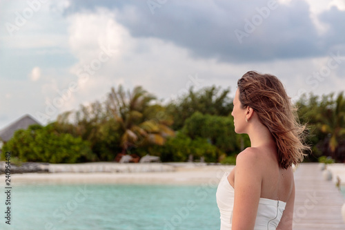 young woman in honeymoon relaxes on a pier looking at the sunset.