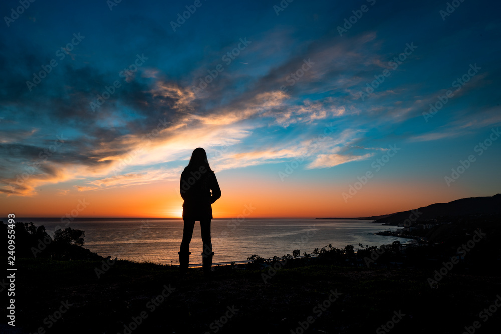 Woman silhouette stares at sunset and ocean
