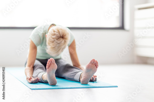 Mature woman in joga pose exercise in appartment at rug with window on background