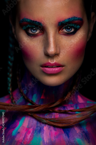 Fashion portrait of beautiful young woman with bright pink and blue colors, art make-up, face art on dark background