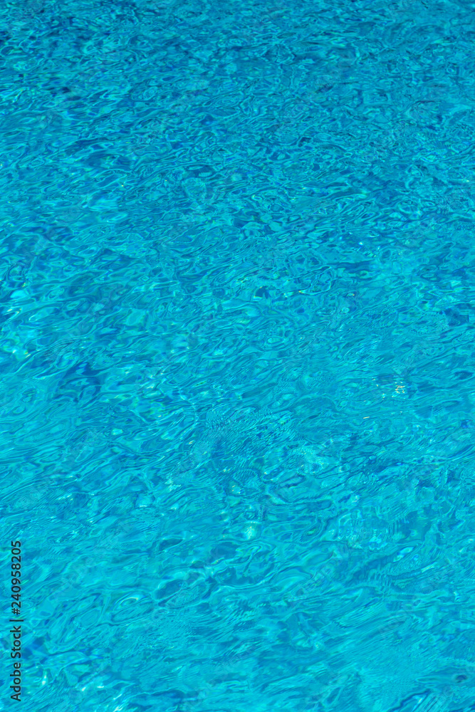 Blue water in swimming pool background. Ripple Water in swimming pool with sun reflection. Blue swimming pool rippled water detail. vertical photo. Blue water in swimming pool background. Ripple Water in swimming pool with sun reflection. Blue swimming pool rippled water detail. vertical photo.