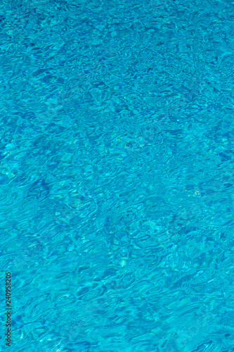 Blue water in swimming pool background. Ripple Water in swimming pool with sun reflection. Blue swimming pool rippled water detail. vertical photo.