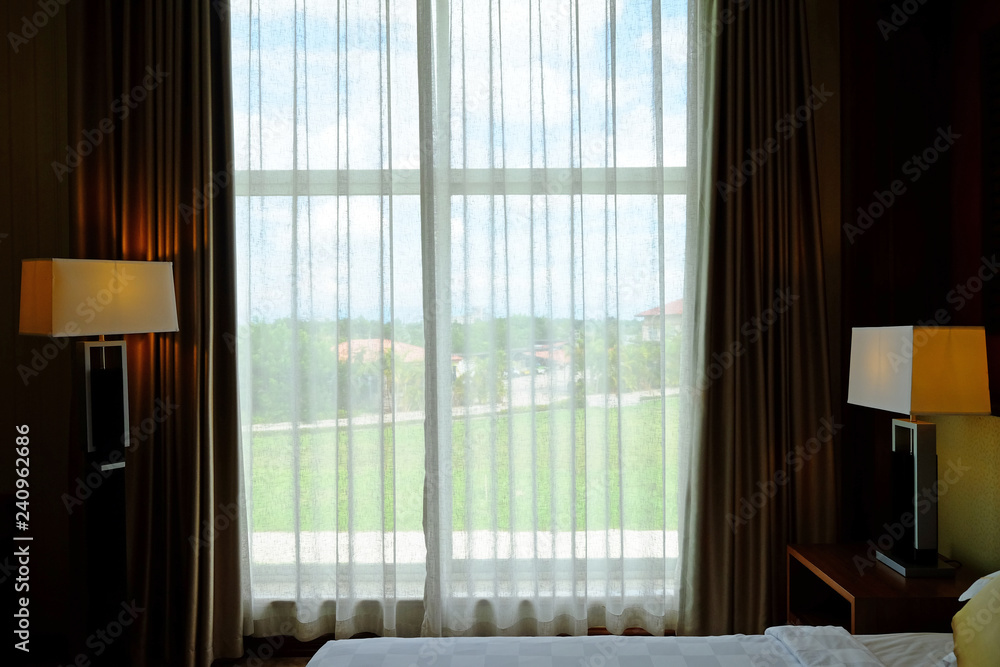 White curtain at window in a bedroom to green garden outside