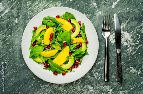 salad with avocado, arugula, spinach, pomegranate, seeds on a concrete background