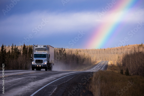 Cube semit truck on wet asphalt road with colorful rainbow over late fall forest landscape after rain in Yukon Territory, YT, Canada