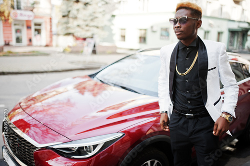Chic handsome african american man in white suit against red luxury car.