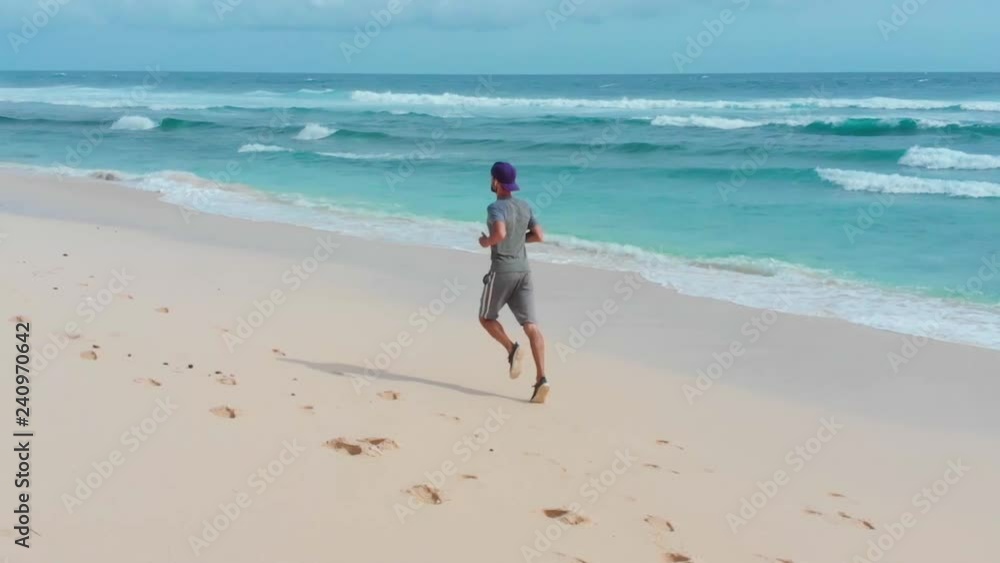 young dynamic athlete runner man with phone and headphones training on beautiful beach sand running in sport well being and healthy lifestyle concept young dynamic athlete runner man with phone and headphones training on beautiful beach sand running in sport well being and healthy lifestyle concept