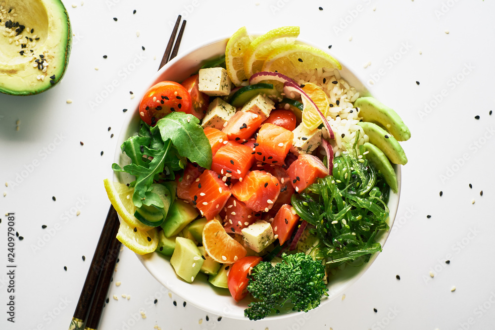 poke bowl with salmon, avocado, cucumber, arugula, broccoli, rice, carrot and sweet onions with chopsticks isolated over white background. top view