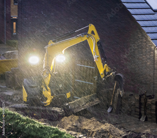 ground worker working at night in bad rainy weather, constructing a garden in the evening