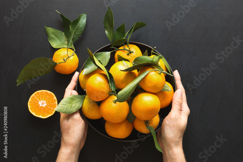 Fresh mandarins with leaves in female hand on black. Healthy eating concept. Copy space.