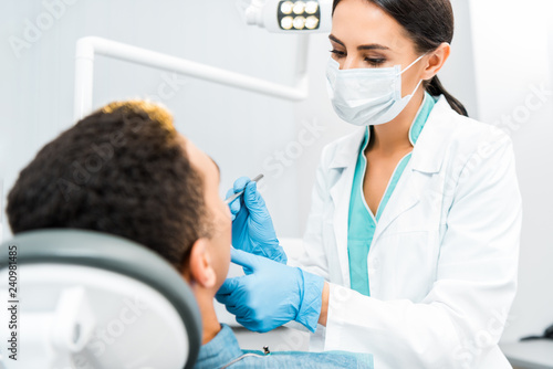 female dentist in mask examining african american patient