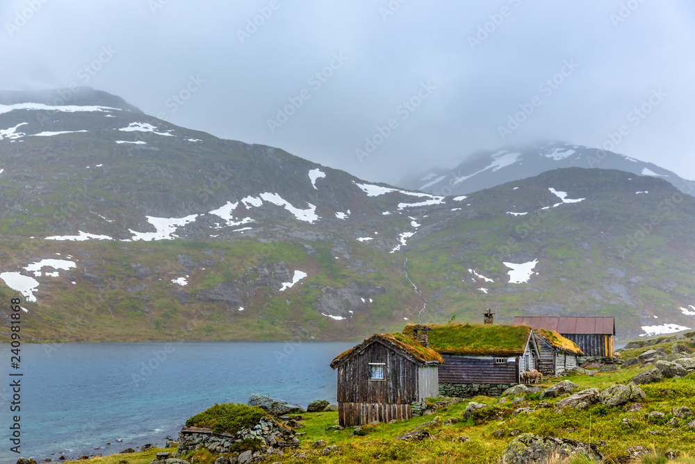 Traditional houses with grass in the roof in front of a lake in a cloudy fog day in Norway