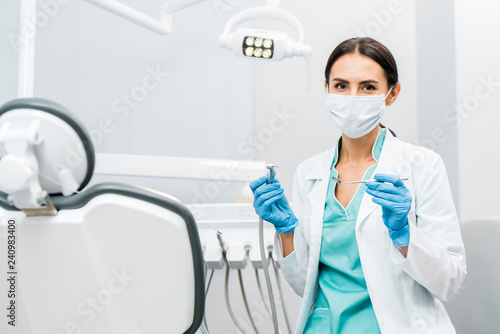 female dentist in white coat and mask holding dental instruments