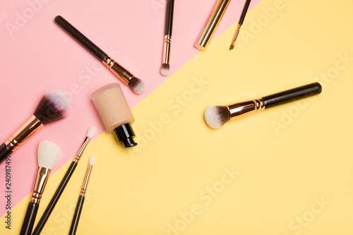 Professional makeup products with cosmetic beauty products, blushes, eye liner, eye lashes, brushes and tools on pink and yellow background