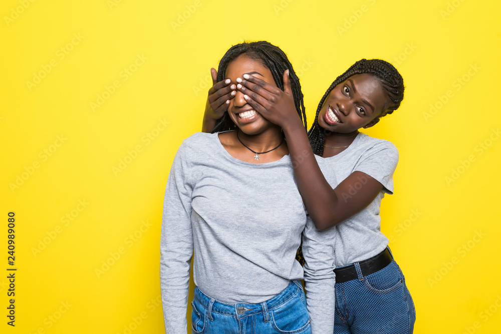 Portrait of two young african women make surprise and cover eyes isolated on yellow background Portrait of two young african women make surprise and cover eyes isolated on yellow background