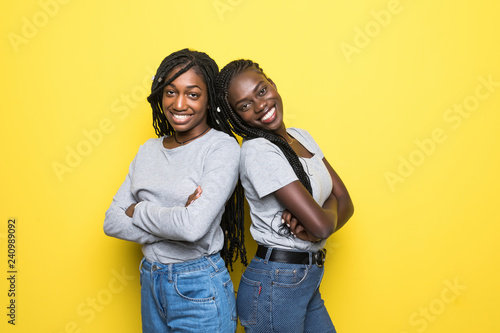 Two african woman standing back to back isolated on yellow background