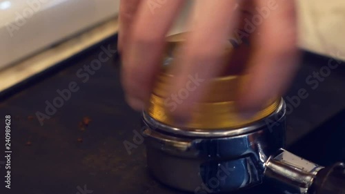 Hand of barista using tamper to press ground coffee into portafilter to make espresso coffee