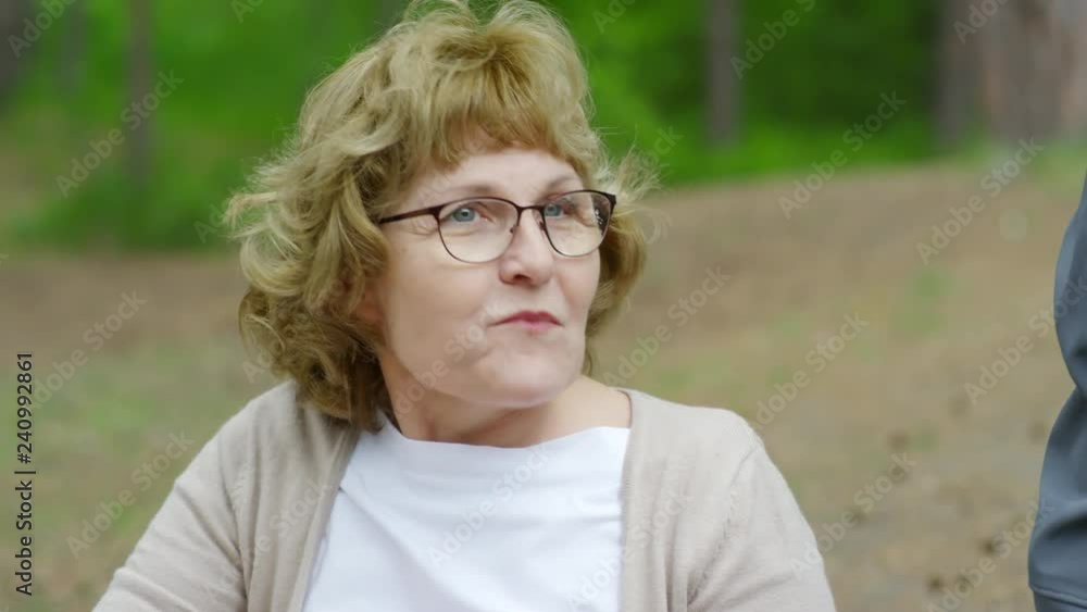 Tilt up shot of cheerful senior woman eating sandwich and chatting with friend on camera while having picnic in forest Tilt up shot of cheerful senior woman eating sandwich and chatting with friend on camera while having picnic in forest