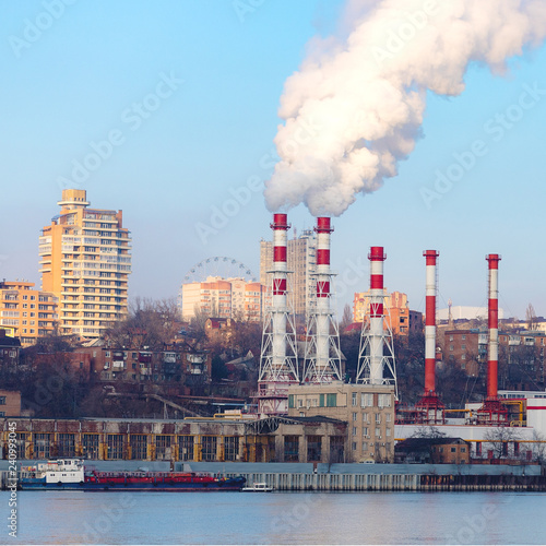 The plant emits pollutants into the atmosphere, from the factory pipes comes out a thick smoke.the pipes emit steam on the background of the city