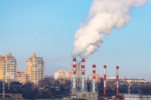 The plant emits pollutants into the atmosphere  from the factory pipes comes out a thick smoke.the pipes emit steam on the background of the city