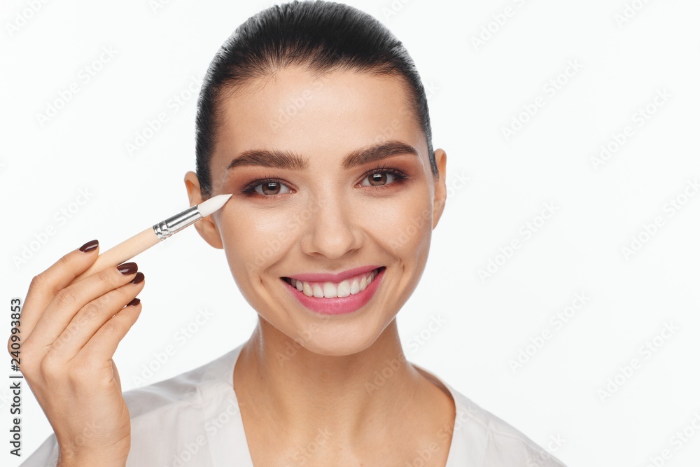 Portrait of a beautiful smiling young woman holding in her hand a white brush for makeup correction