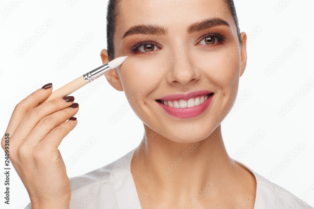 Portrait of a beautiful smiling young woman holding in her hand a white brush for makeup correction