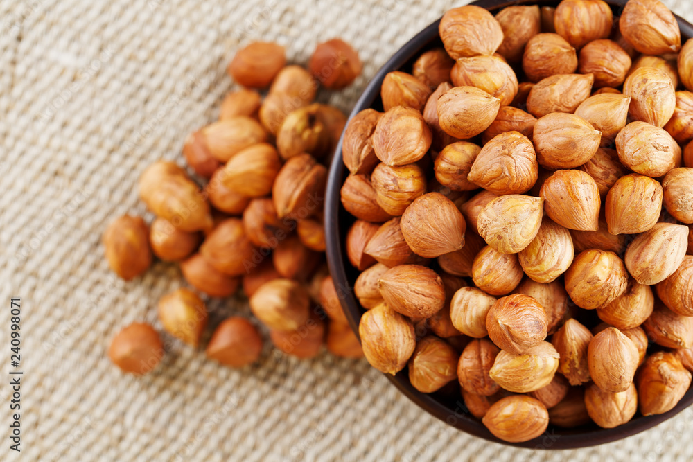 Peeled hazelnuts in a wooden, dark brown cup on a burlap cloth. Super Food, Raw. Peeled hazelnuts in a wooden, dark brown cup on a burlap cloth. Super Food, Raw.