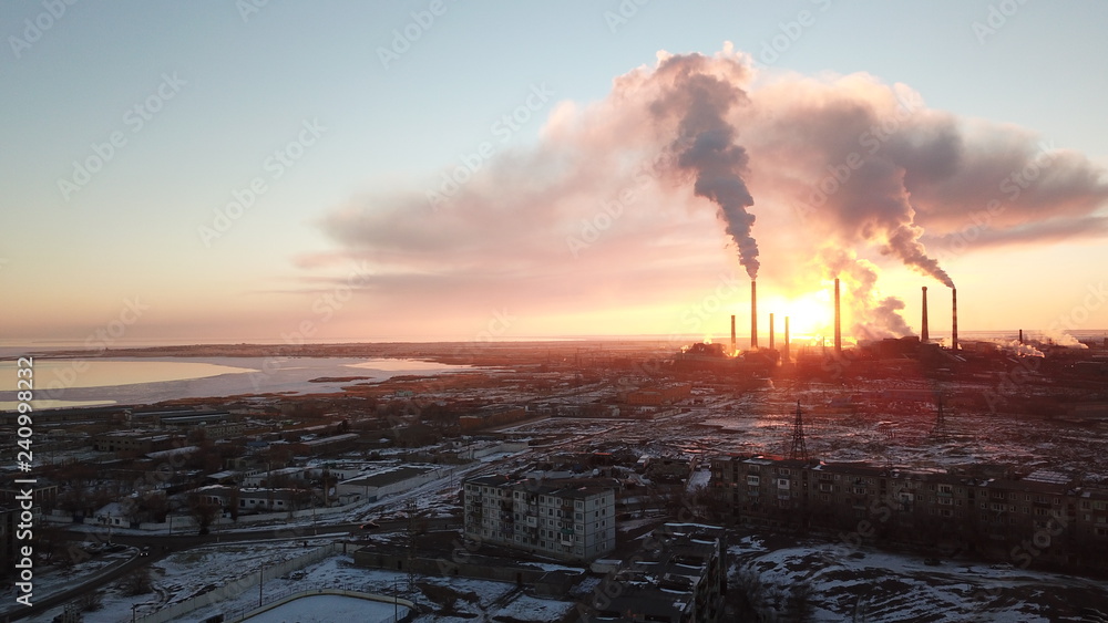 Epic sunset on the background of a Smoking factory. The red sun with bright rays goes beyond the pipe factories and smog. Shooting with the drone. View of part of the city, lake and industry. Red sky. Epic sunset on the background of a Smoking factory. The red sun with bright rays goes beyond the pipe factories and smog. Shooting with the drone. View of part of the city, lake and industry. Red sky.