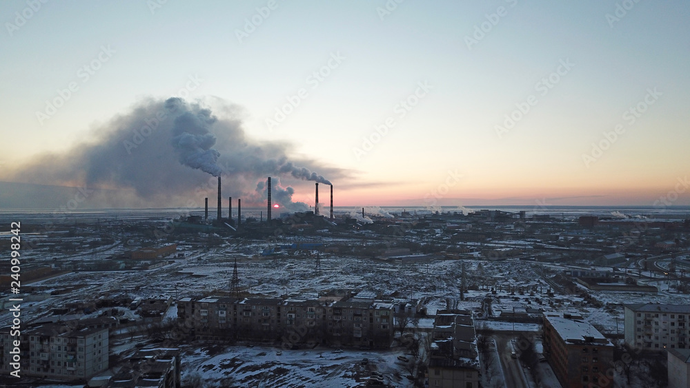 Epic sunset on the background of a Smoking factory. The red sun with bright rays goes beyond the pipe factories and smog. Shooting with the drone. View of part of the city, lake and industry. Red sky.