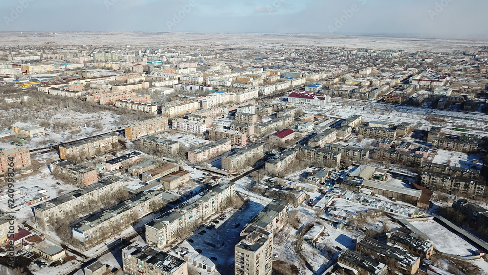 Aerial view of the drone on a small town. Winter season. Low five-storey houses. Soviet construction. The city among the desert. In the center of the cities much TV tower is worth. Small street.