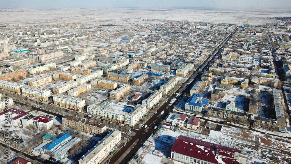 Aerial view of the drone on a small town. Winter season. Low five-storey houses. Soviet construction. The city among the desert. In the center of the cities much TV tower is worth. Small street.