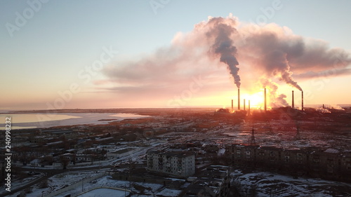 Epic sunset on the background of a Smoking factory. The red sun with bright rays goes beyond the pipe factories and smog. Shooting with the drone. View of part of the city, lake and industry. Red sky.