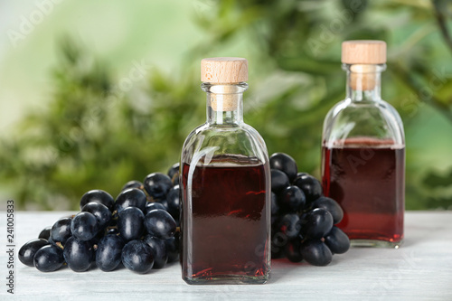 Bottles with wine vinegar and fresh grapes on wooden table against blurred background