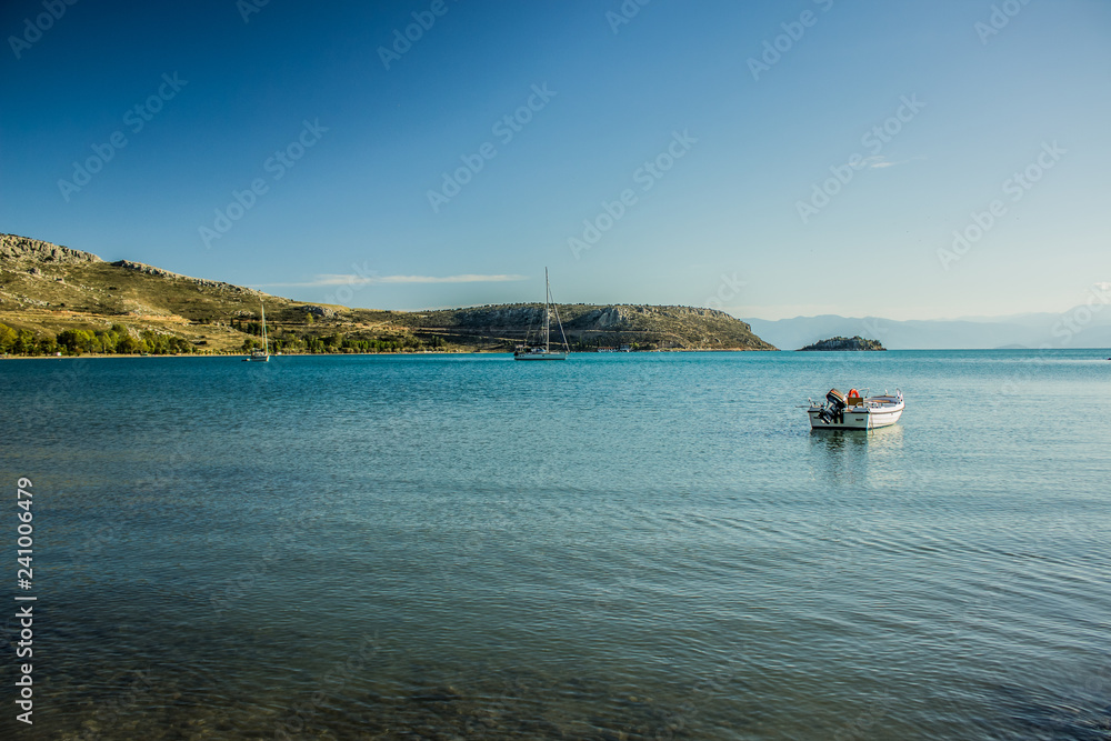 Obraz premium cozy sea bay calm water surface with small empty fishing boat in morning fresh sun rise time, south Europe scenic natural landscape